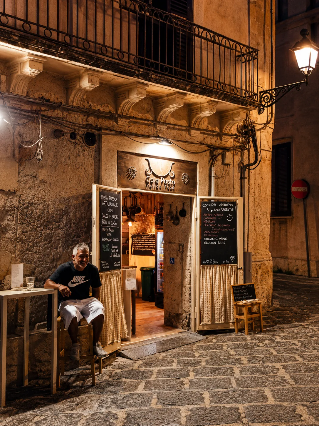 The warmly lit ColaPasta entrance and handwritten menu boards on a stone street at night.