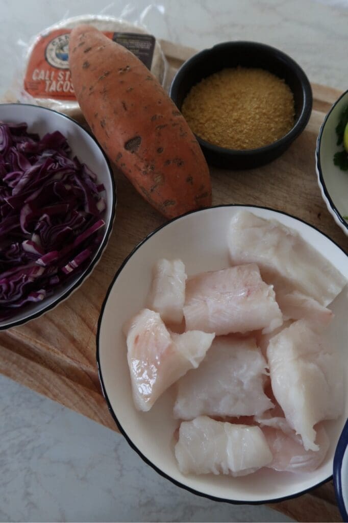 Taco assembly scene with bowls of slaw, crispy cod pieces, and chilli crema.