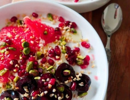 Overhead shot of a breakfast bowl with yoghurt, cherries, grapefruit, and pistachios layered in a ceramic dish